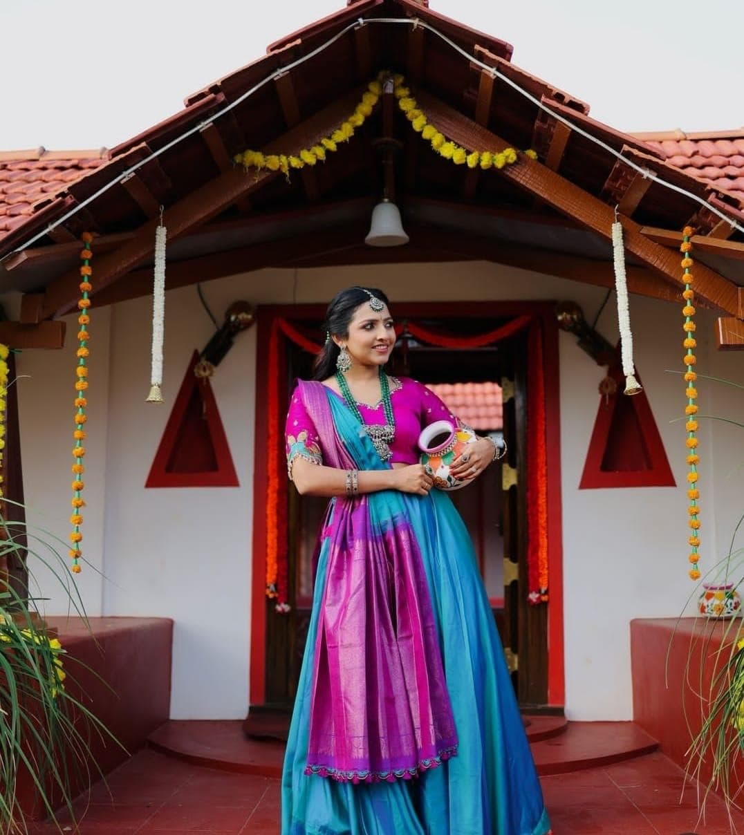 A guest in a silk half-saree at the marigold-garlanded cottage entrance