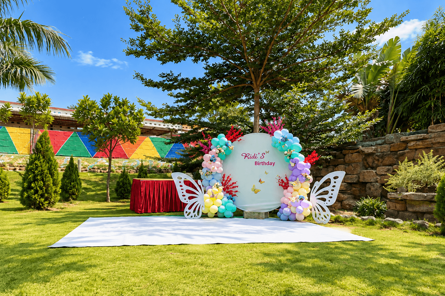 A floral balloon arch and butterfly backdrop for a birthday on the lawn